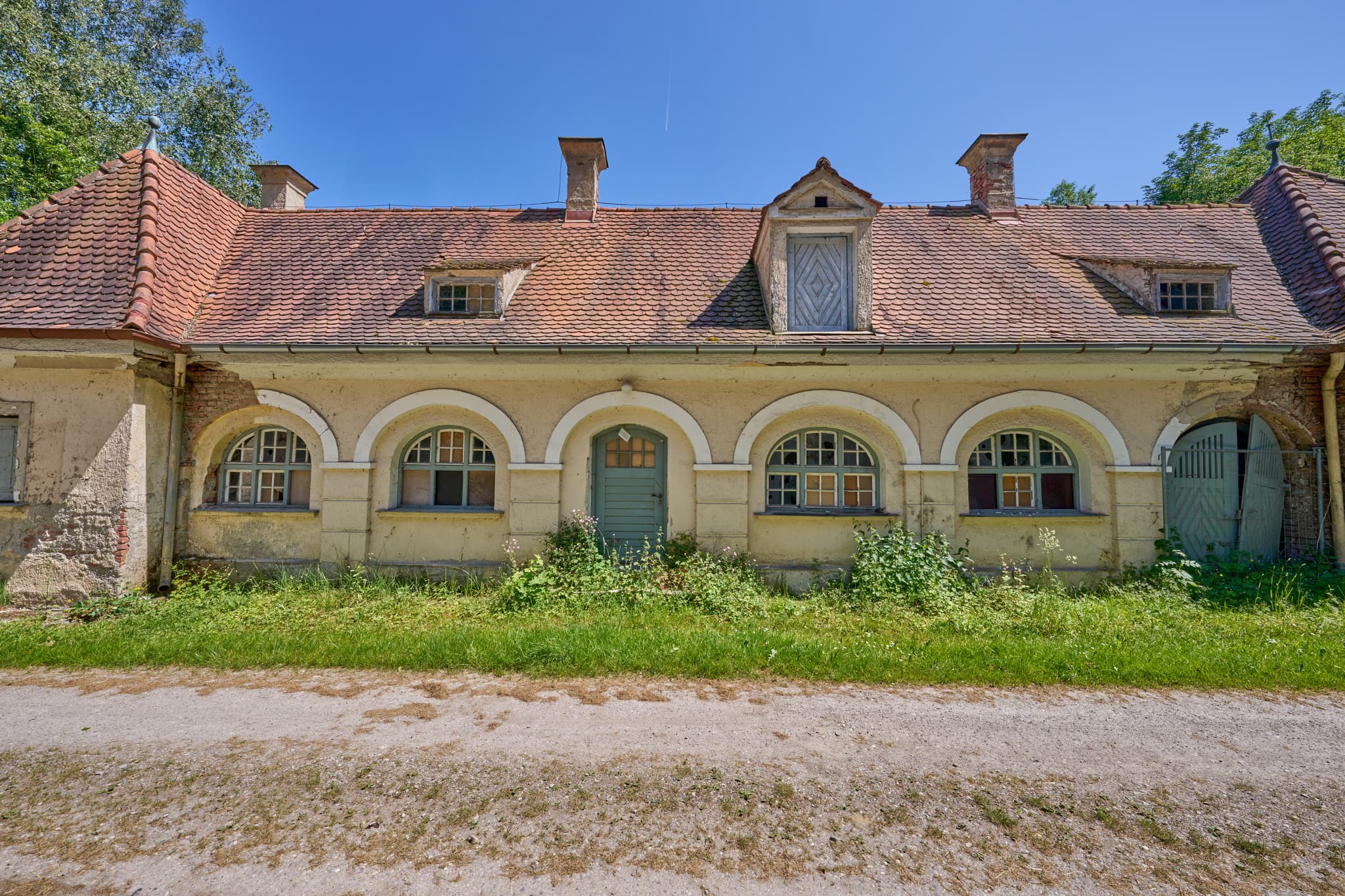 Alte Wäscherei in Ecksberg, Oberbayern, Inn-Salzach - Alte Wäscherei Ecksberg, Mühldorf am Inn, Oberbayern. Historisches Gebäude der Region Inn-Salzach. Zeigt Rundbogenfenster, grüne Tür, üppige Vegetation.