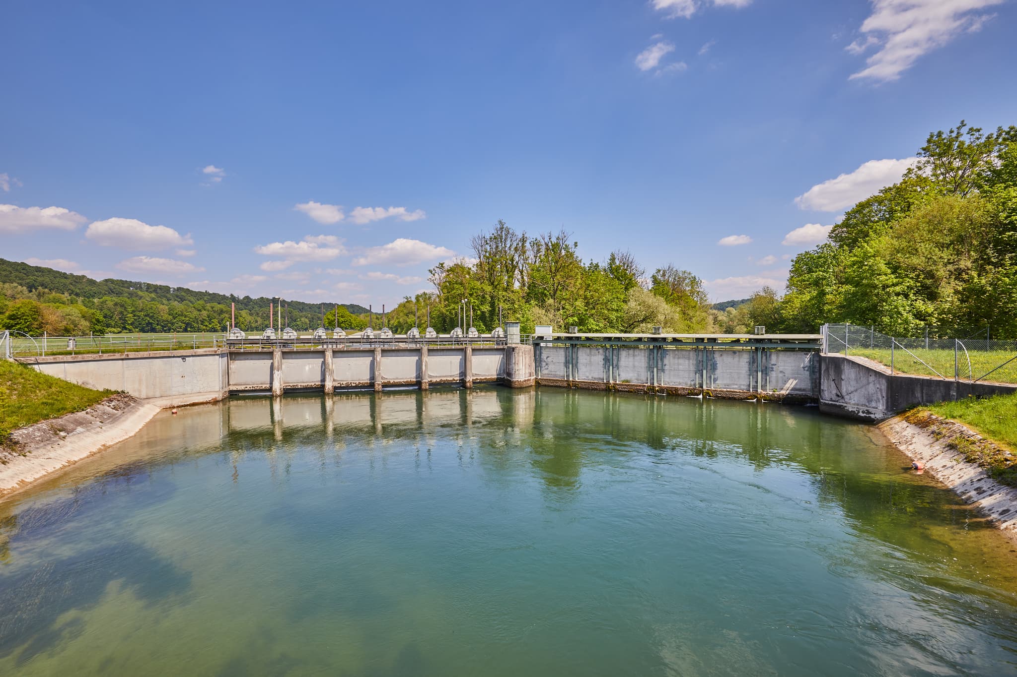 Alzschleuse, Burgkirchen-Hirten Alz Radweg, Burgkirchen - Ein Wehr am Alz Radweg in Burgkirchen, Altötting, Oberbayern, Inn-Salzach. Die Wasserlandschaft in Deutschland zeigt grüne Ufer, Bäume unter blauem Himmel.