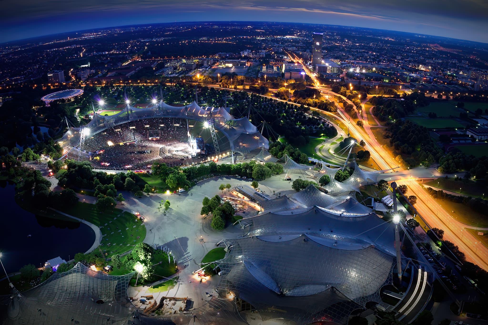 Aussicht Olympiaturm, Olympiapark, Olympiastadion, München - Olympiapark und Olympiastadion in München, Deutschland. Nachtaufnahme mit beleuchteter Architektur, Konzerten, Panorama