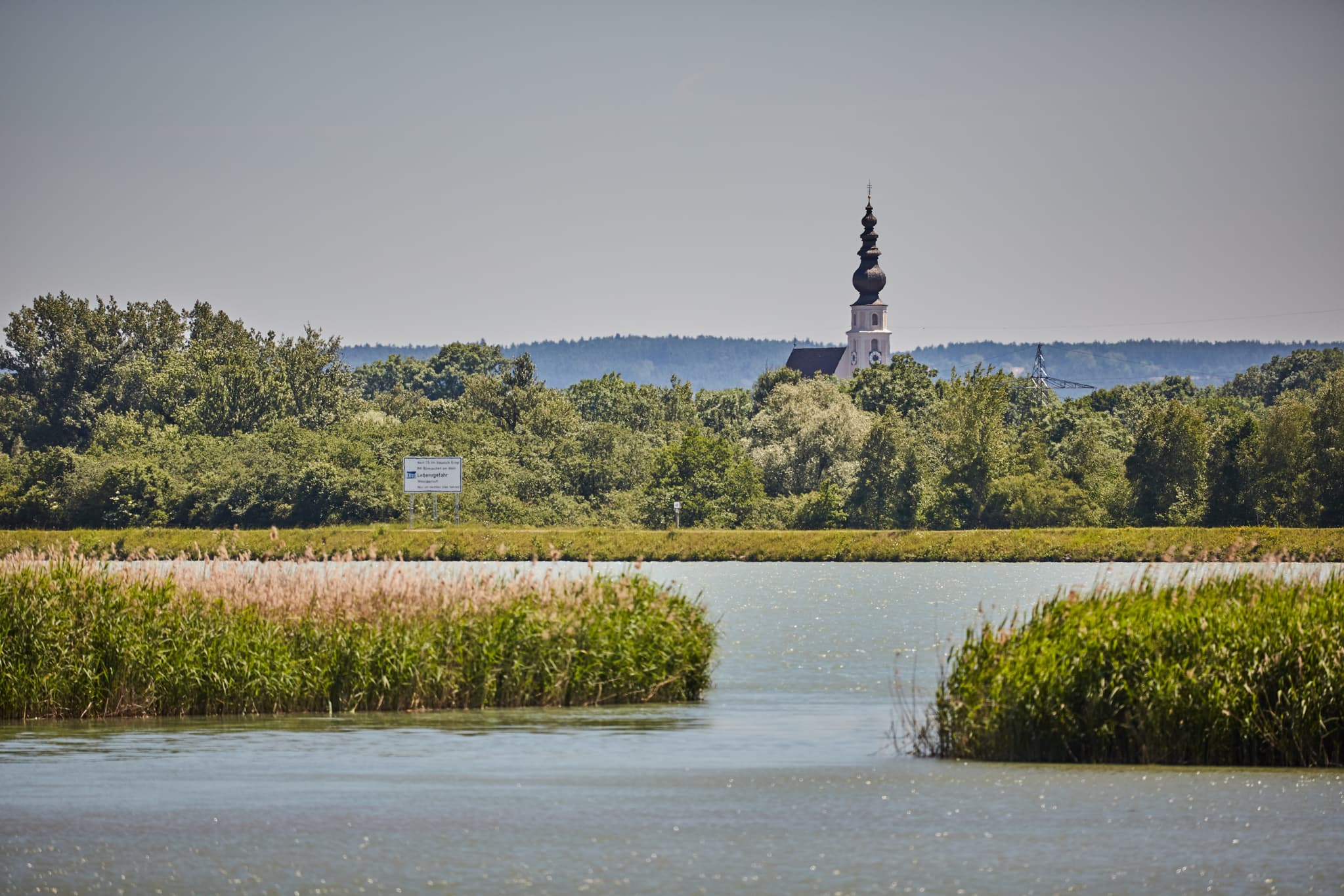 Aussichtsturm, Unterer Inn Blick nach Mining, Ering am Inn - Panoramablick über den Inn bei Ering am Inn, Rottal-Inn, Niederbayern. Die Landschaft zeigt Fluss, Schilf, Bäume und die Kirche in Mining.