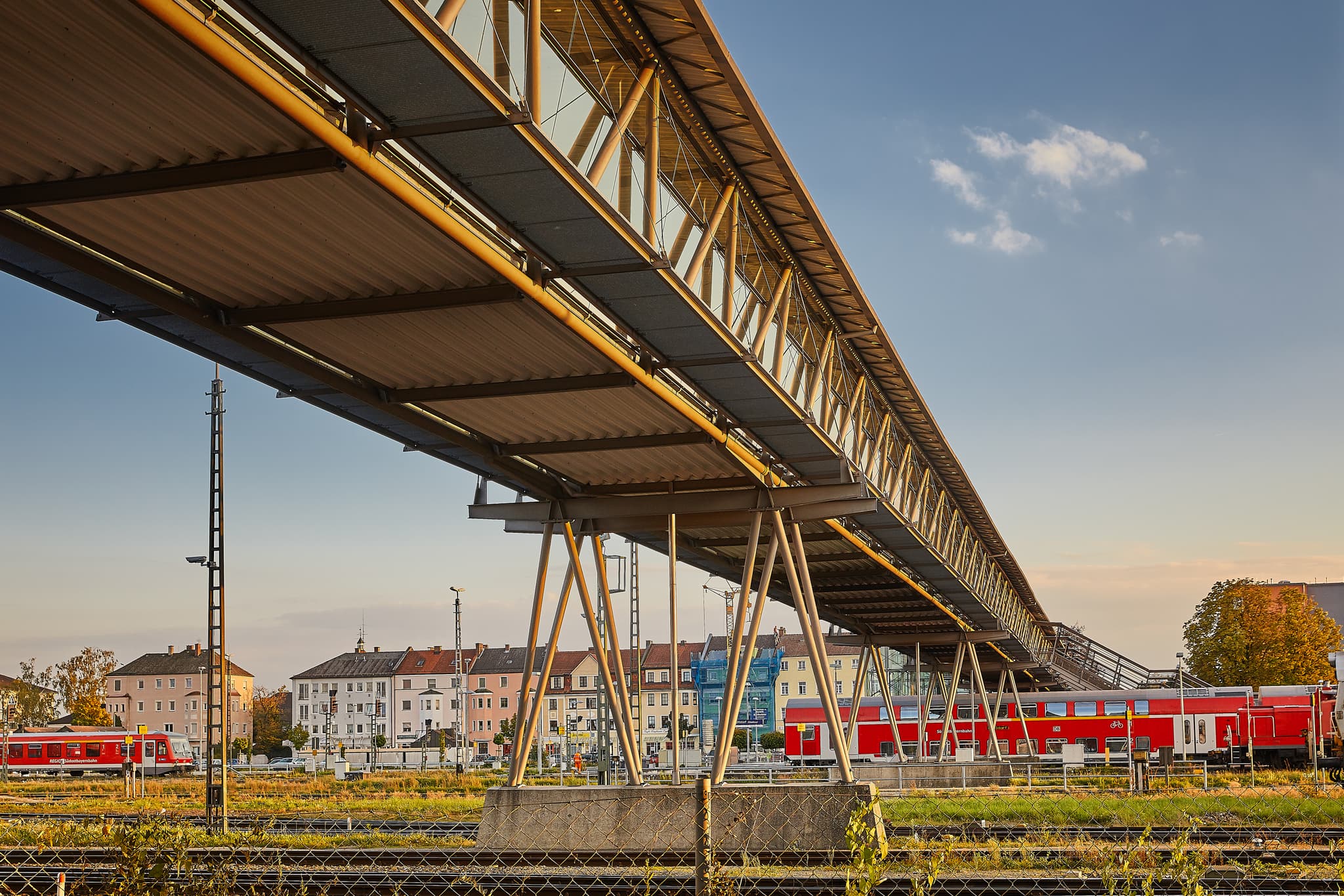 Bahnhof Unten, Mühldorf am Inn, MÜ, Oberbayern, Inn-Salzach - Fußgängerbrücke und Bahngleise am Bahnhof Mühldorf, Mühldorf am Inn, Oberbayern, Inn-Salzach, Deutschland. Rote Züge und Gebäude prägen die städtische Szenerie.
