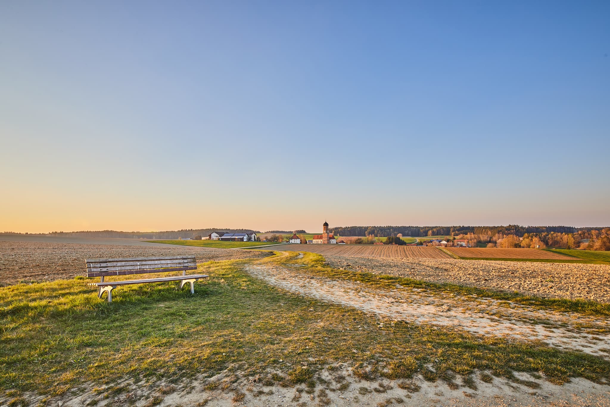 Bank mit Aussicht, Landschaft Martinskirchen, Rogglfing - Weite Landschaft mit Bank und Dorf im Hintergrund bei Martinskirchen Rogglfing, Wurmannsquick, Landkreis Rottal-Inn, Niederbayern, Deutschland.