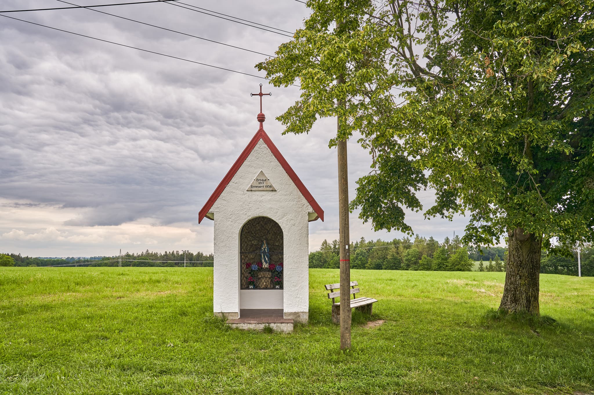 Bildstock Kapelle, Höresham, Altötting, Oberbayern - Kapelle Höresham, Burgkirchen, Altötting, Oberbayern. In grüner Wiesenlandschaft Inn-Salzach, Deutschland. Baum & Bank unter bewölktem Himmel.