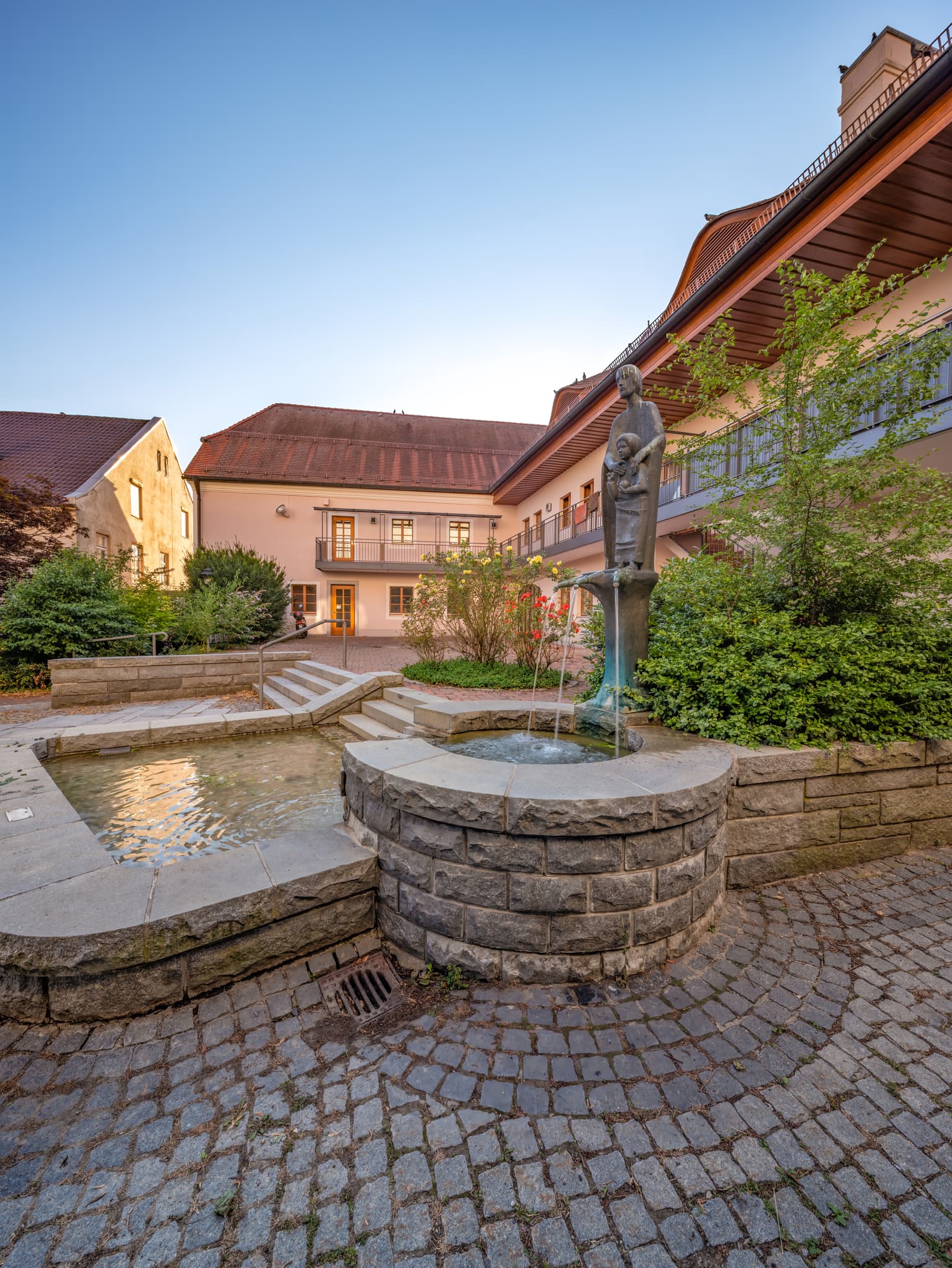 Brunnen, Pfarrkirche, Bad Griesbach, Passau - Steinbrunnen mit einer Marienstatue auf Kirchenplatz der Pfarrkirche in Bad Griesbach, Landkreis Passau, Niederbayern, Inn-Salzach, Bayern, Deutschland.
