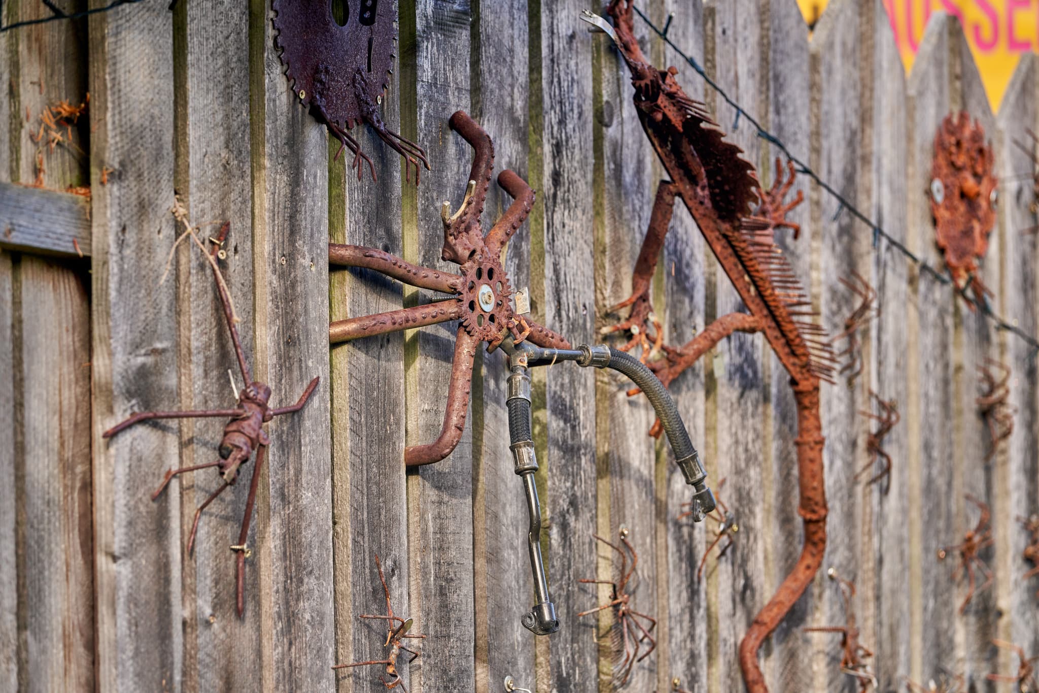 Der Zaun ist Teil des Hörniweg in Schönau, Rottal-Inn - Detailaufnahme eines Zauns mit rostigen Metallskulpturen am Hörniweg in Schönau, Rottal-Inn, Niederbayern, Holzland, Deutschland.