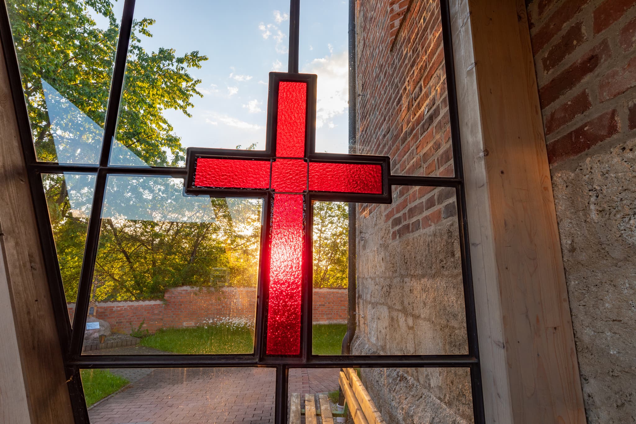 Filialkirche St. Rupert, Gumpersdorf, Rottal, Niederbayern - Kirchenfenster, rotes Kreuz. Blick auf Kirche Gumpersdorf, Zeilarn, Rottal-Inn, Niederbayern. Holzland, Deutschland. Mauerwerk, Grünflächen, Weg im Sonnenlicht.