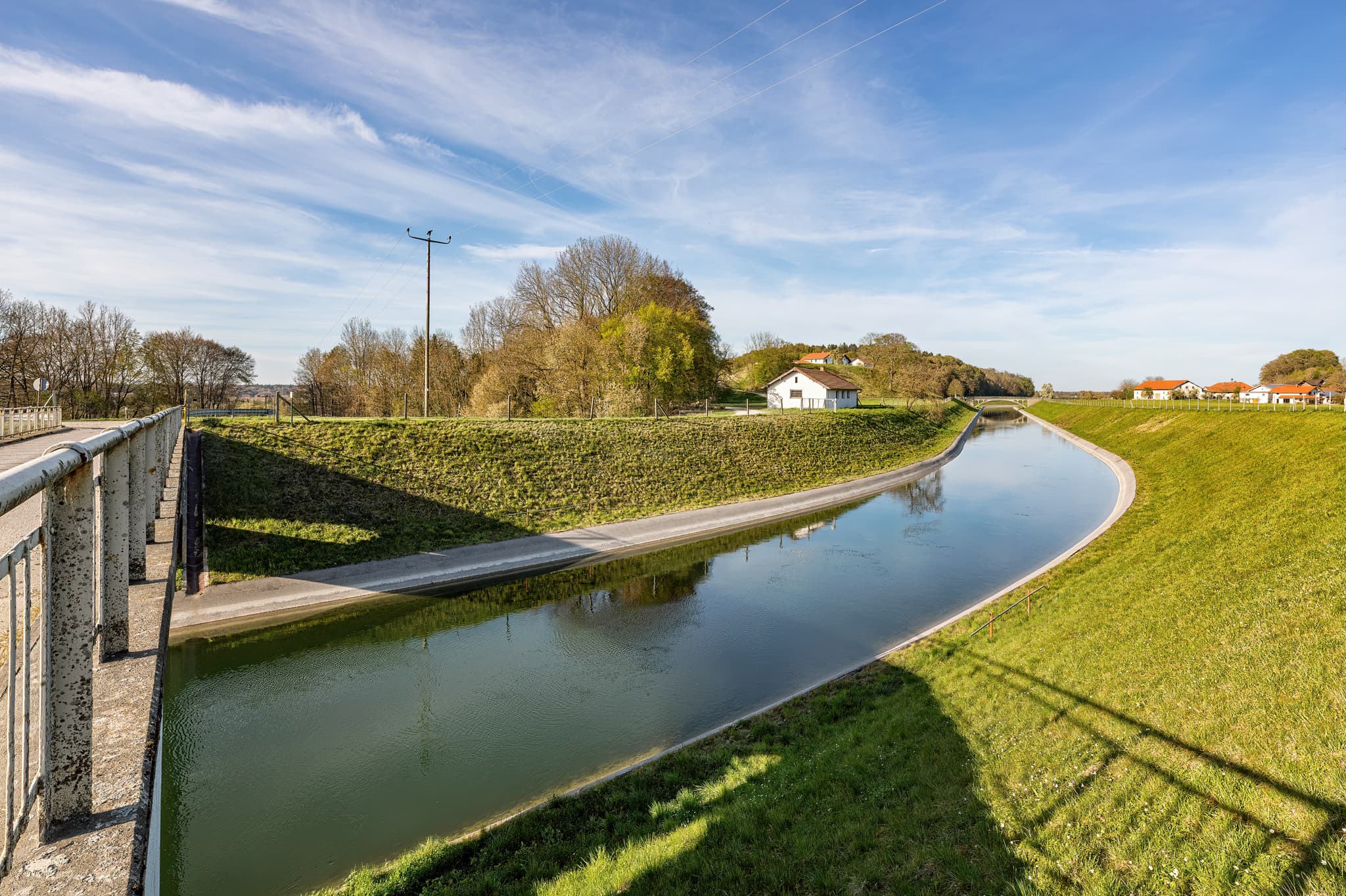 Idyllischer Alzkanal bei Eschlberg, Altötting, Oberbayern - Der Alzkanal in Eschlberg, Mehring, Landkreis Altötting, Oberbayern. Landschaft der Inn-Salzach-Region in Deutschland mit Wasserlauf, grünen Ufern und Gebäuden.