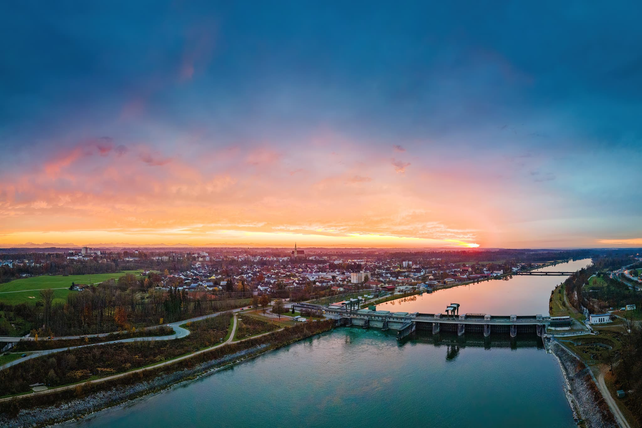 Inn-Kraftwerk am Abend in Neuötting, Oberbayern, Inn-Salzach - Sonnenuntergang über Neuötting, Landkreis Altötting, Oberbayern. Panorama des Inns mit Wehr und Stadtansicht bei Dämmerung.
