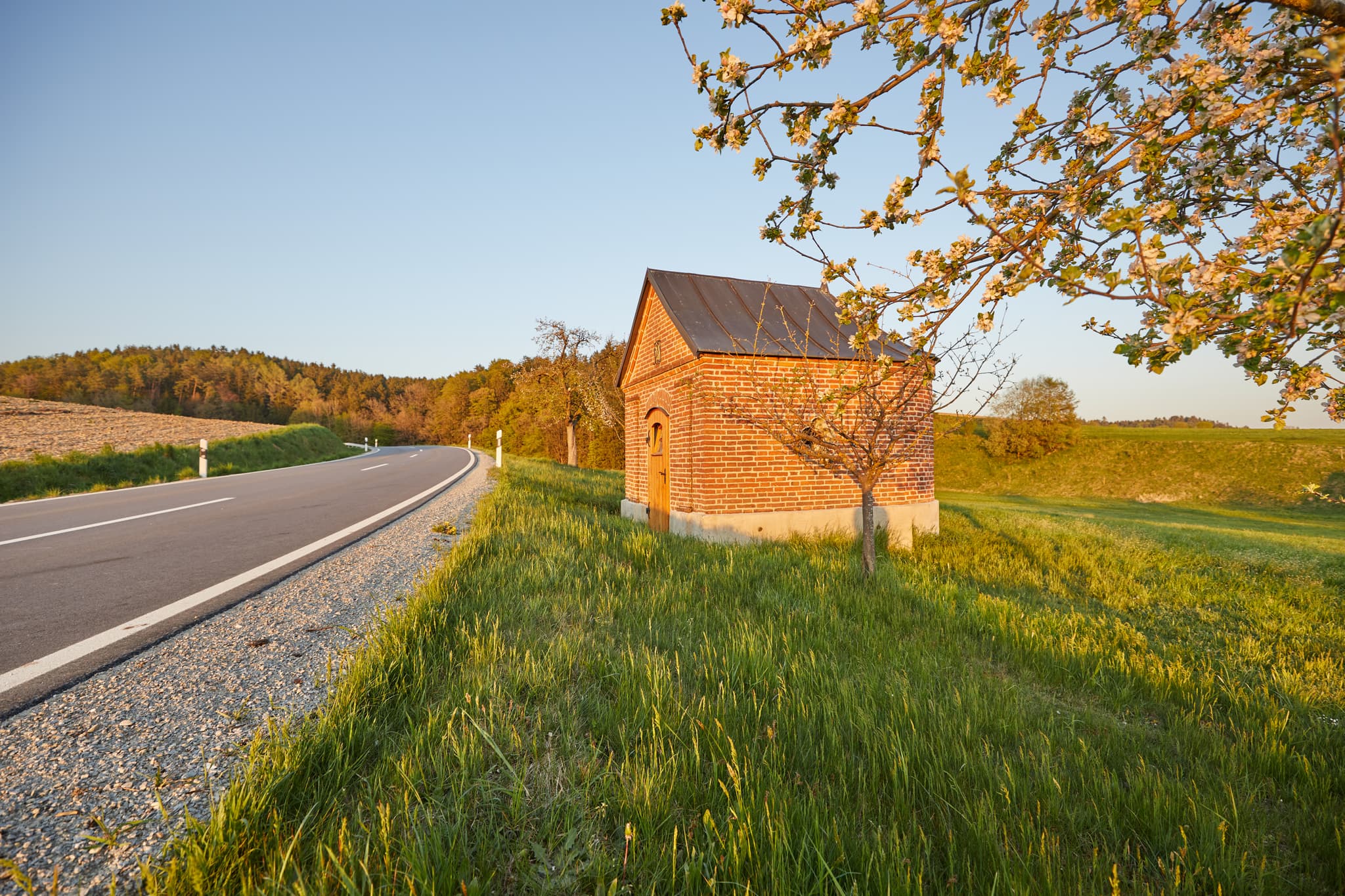 Kapelle an der Tanner Straße nach Schildthurn, Niederbayern. - Kleine Backsteinkapelle im Abendlicht in Schildthurn bei Zeilarn, Landkreis Rottal-Inn, Niederbayern, Deutschland. Umgeben von grünen Wiesen und Bäumen.