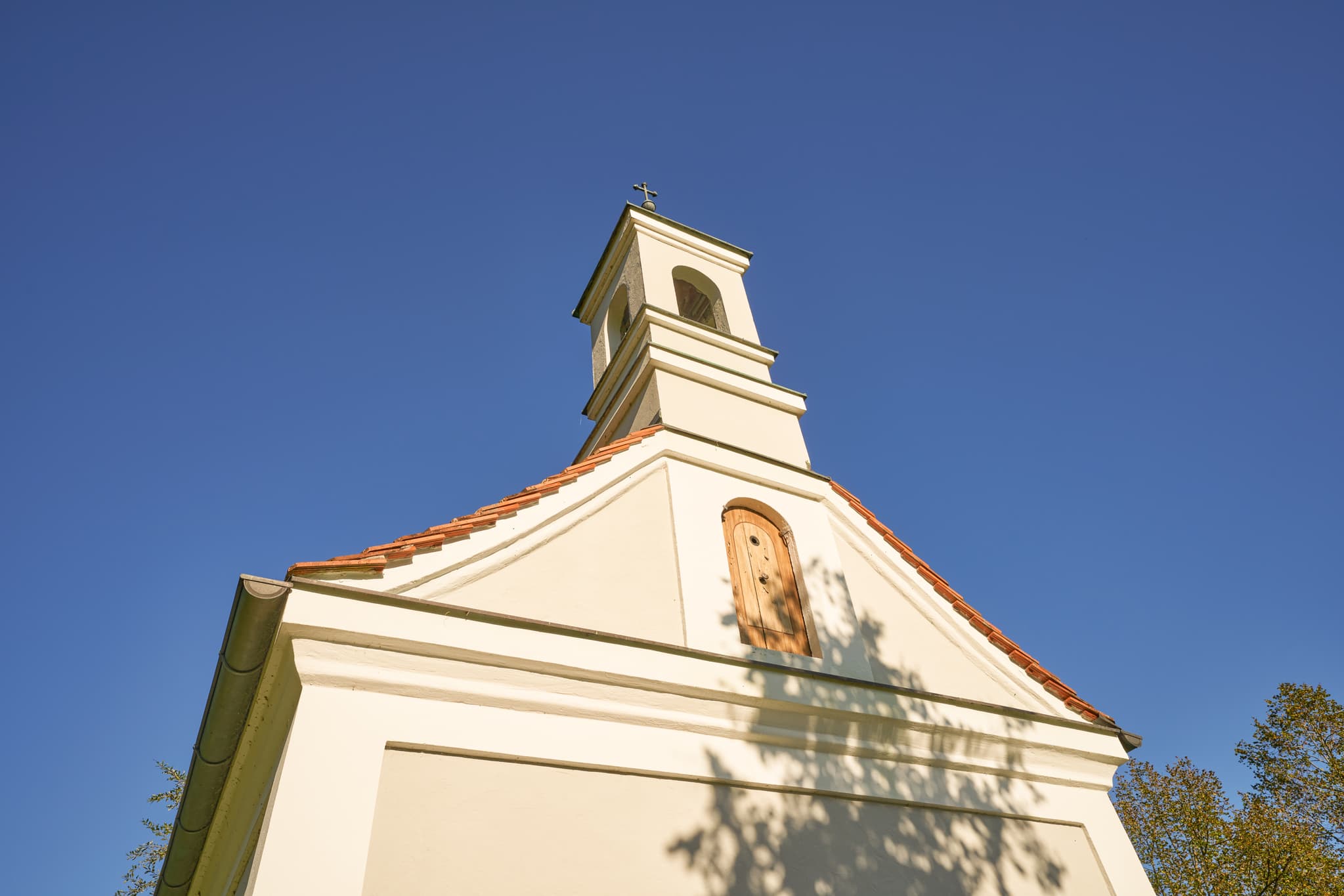 Kapelle Ecksberg Altmühldorf, Mühldorf am Inn, Oberbayern - Kapelle in Ecksberg Altmühldorf Kronwidl, Mühldorf am Inn, Oberbayern, Inn-Salzach, Deutschland. Darstellung des Bauwerks mit Baumschatten unter blauem Himmel.