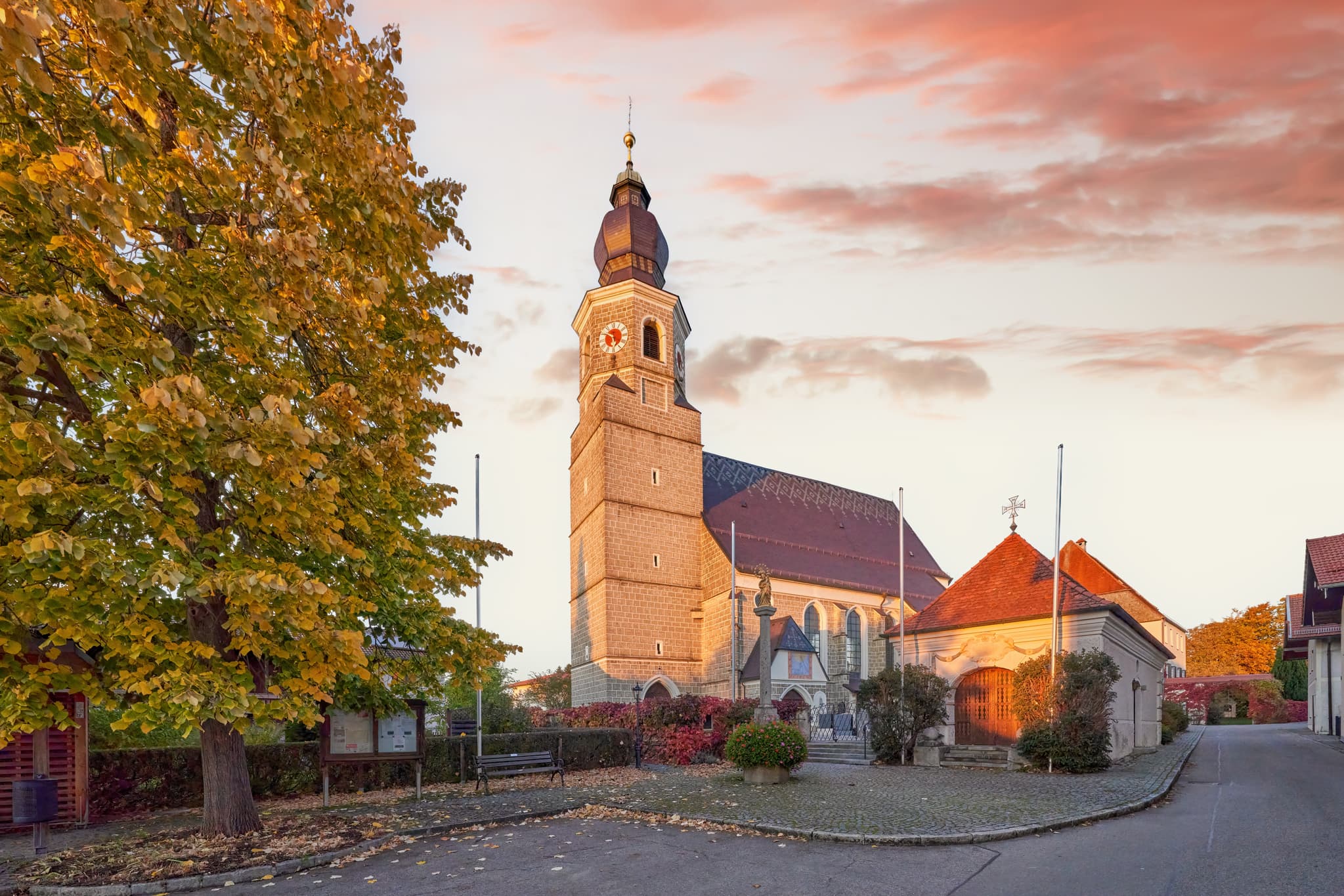 Kirche Feichten, Altötting, Oberbayern, Inn-Salzach - Kirche Mariä Himmelfahrt in Feichten, Altötting, Oberbayern, Inn-Salzach. Herbstlaub am Baum, rötlicher Himmel. Friedliche Szene.