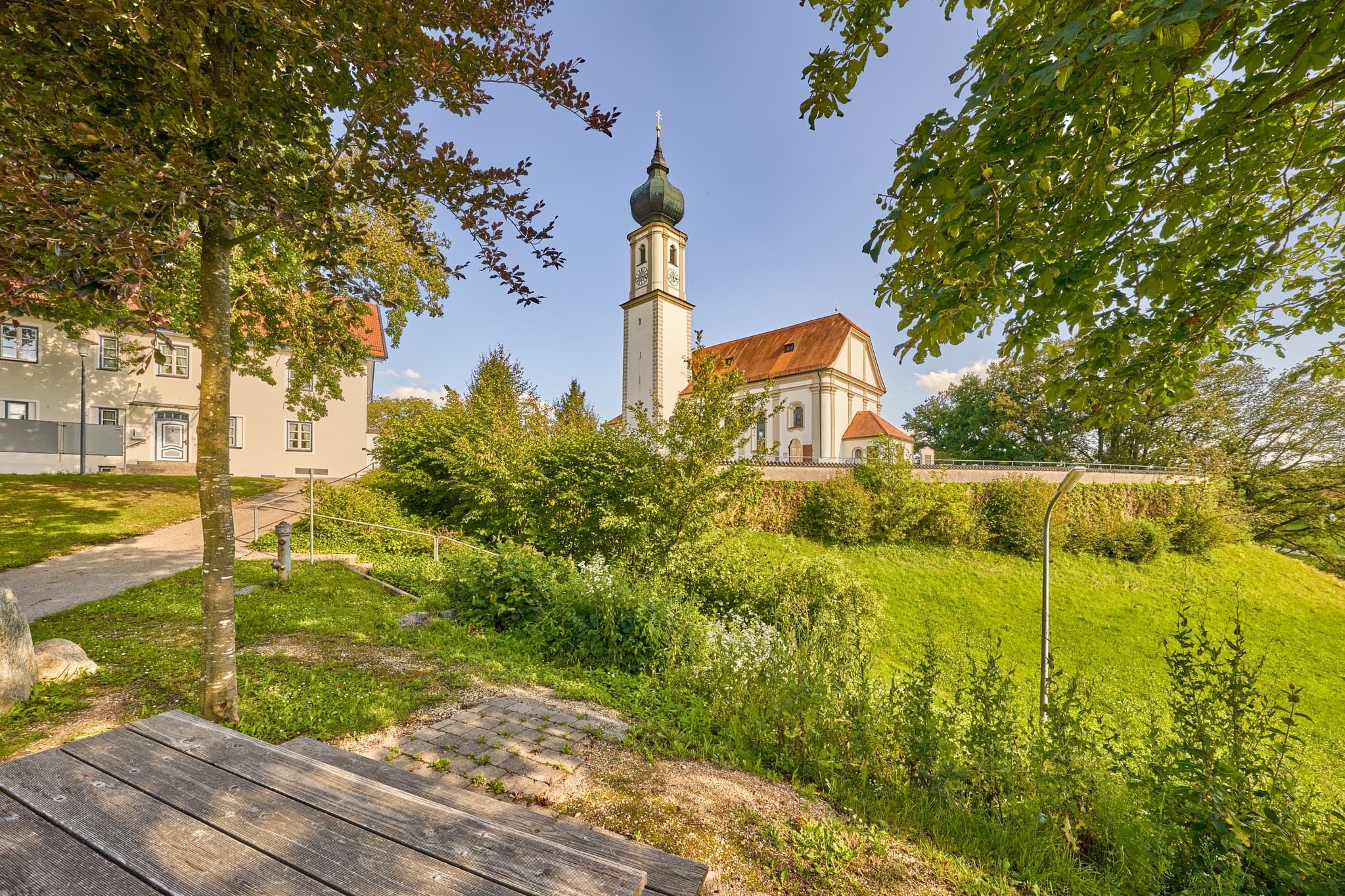 Kirche St. Martin, Niedertaufkirchen, Mühldorf, Inn-Salzach - Kirche St. Martin, Niedertaufkirchen, Mühldorf am Inn, Oberbayern, Inn-Salzach. Historisches Gotteshaus mit Zwiebelturm und Mauer. Grüne Wiese, blauer Himmel.