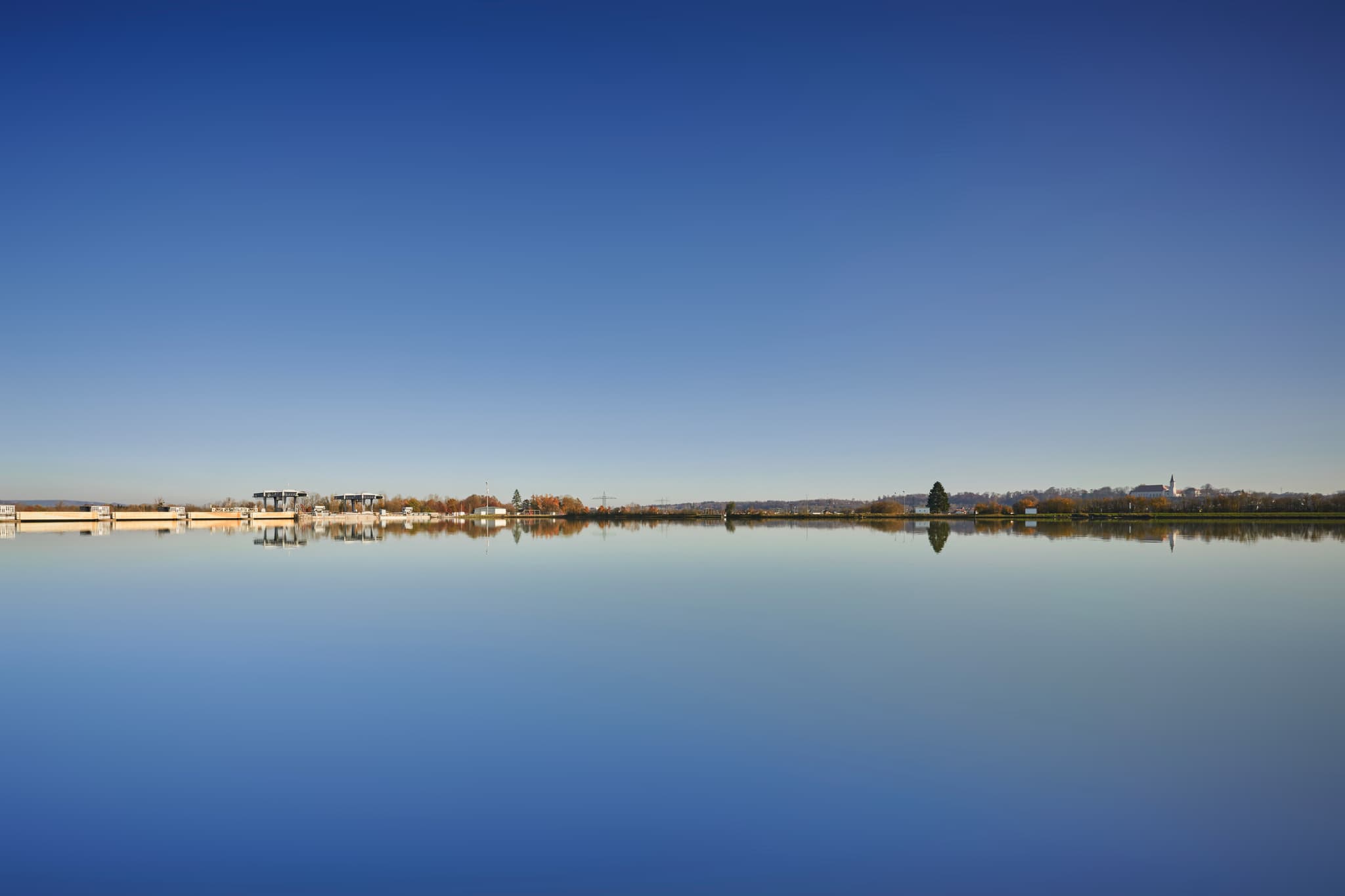 Kraftwerk Simbach-Braunau, Rottal-Inn, Niederbayern - Das Kraftwerk Simbach-Braunau nahe Kirchdorf am Inn, Landkreis Rottal-Inn, Niederbayern. Weite Wasserfläche spiegelt blauen Himmel und Ufer.
