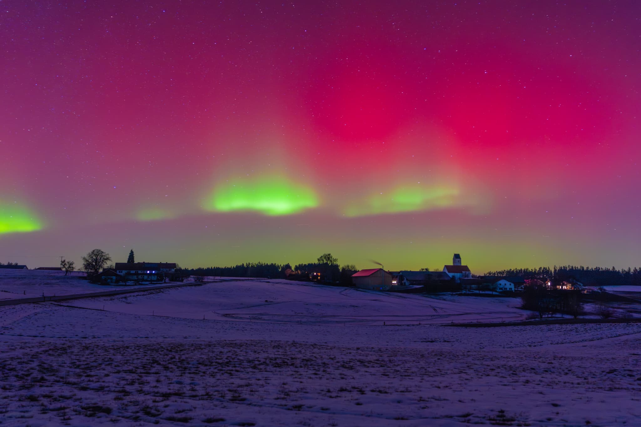 Ortsansicht mit Polarichter 19.01.2026, Ecking, Altötting - Ecking, Reischach, Altötting, Oberbayern, Deutschland. Farbenprächtiges Polarichter,  schneebedeckte Landschaft mit Gebäuden. Eine Winteransicht im Holzland.