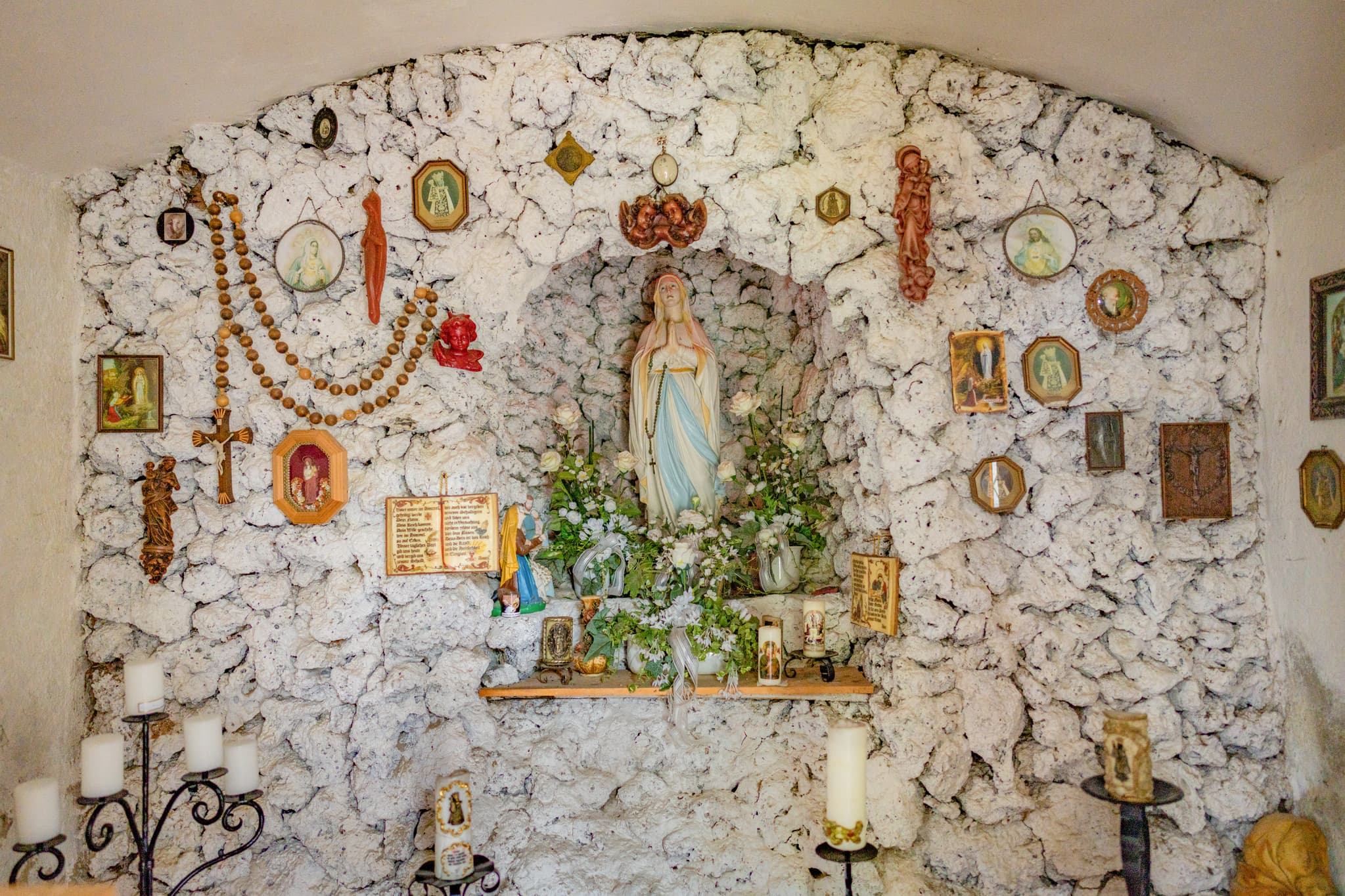 Pfarrkirche St. Ägidius, Roßbach, Mühldorf, Oberbayern - Marienstatue in Kapelle Roßbach, Niedertaufkirchen, Mühldorf am Inn. Kerzen, Rosenkränze, Votivgaben an Steinwand. Religiöse Stätte Oberbayern.