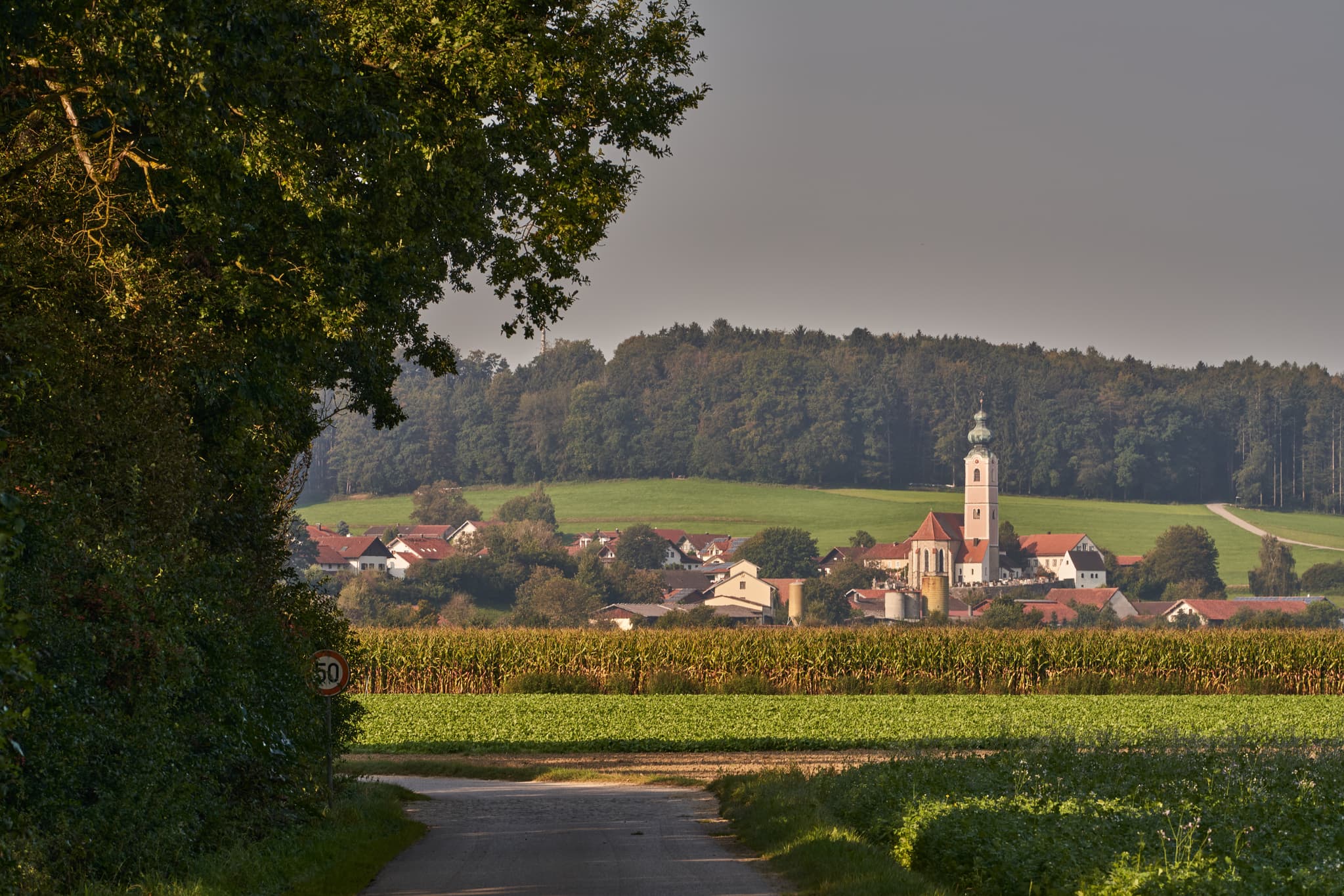 Pilgerweg Richtung Mehring, Badhöring, Altötting, Oberbayern - Ansicht von Badhöring mit Kirche, umgeben von Feldern und Wald. Der Pilgerweg führt durch die Landschaft bei Mehring, Landkreis Altötting, Oberbayern.