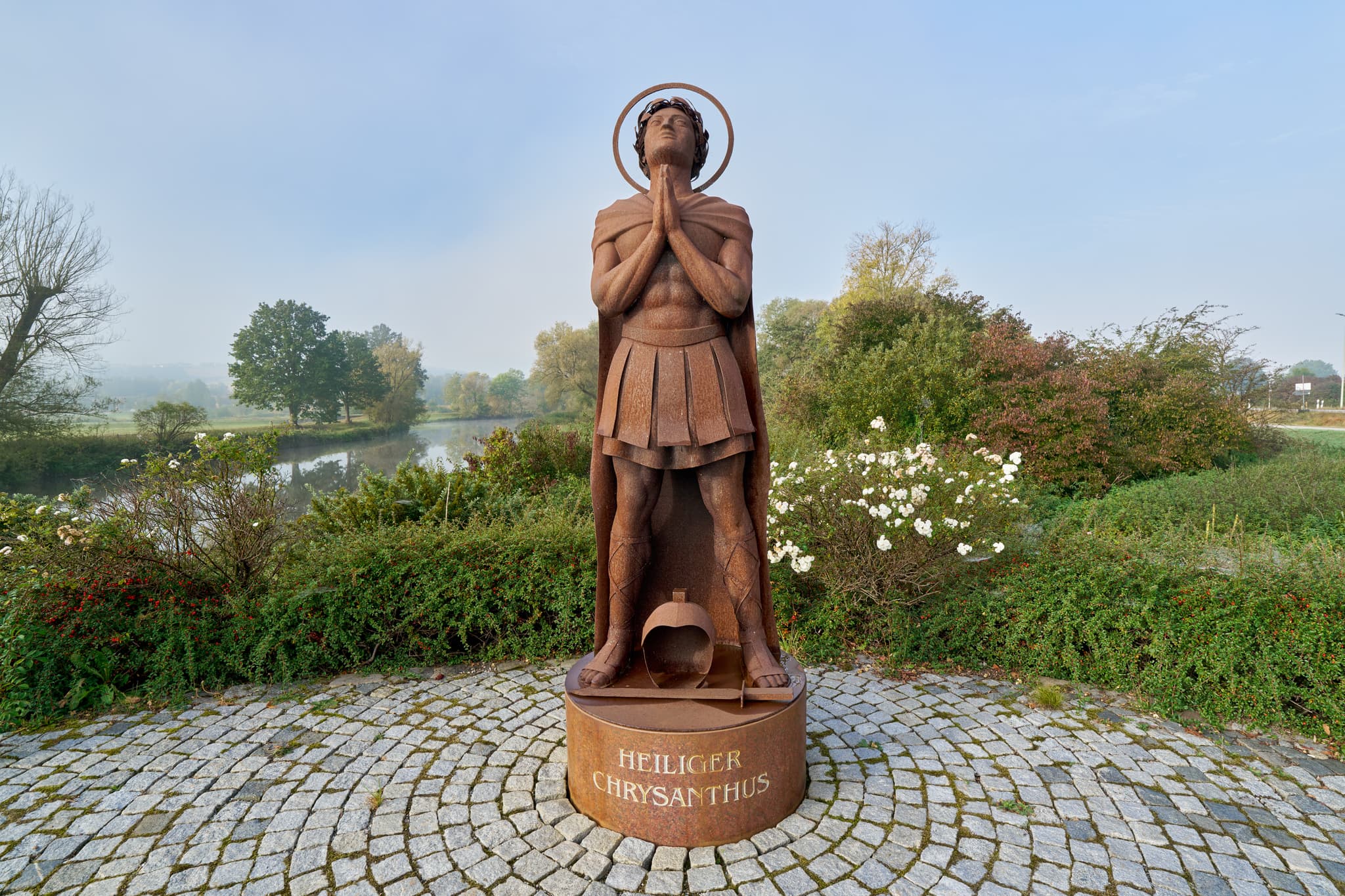 Rott im Herbst, Bad Birnbach, Niederbayern, Bäderdreieck - Statue "Heiliger Chrysanthus" in Bad Birnbach, Rottal-Inn, Niederbayern. Herbstliche Szene am Ufer der Rott im Bäderdreieck, zeigt Figur auf Kopfsteinpflaster.
