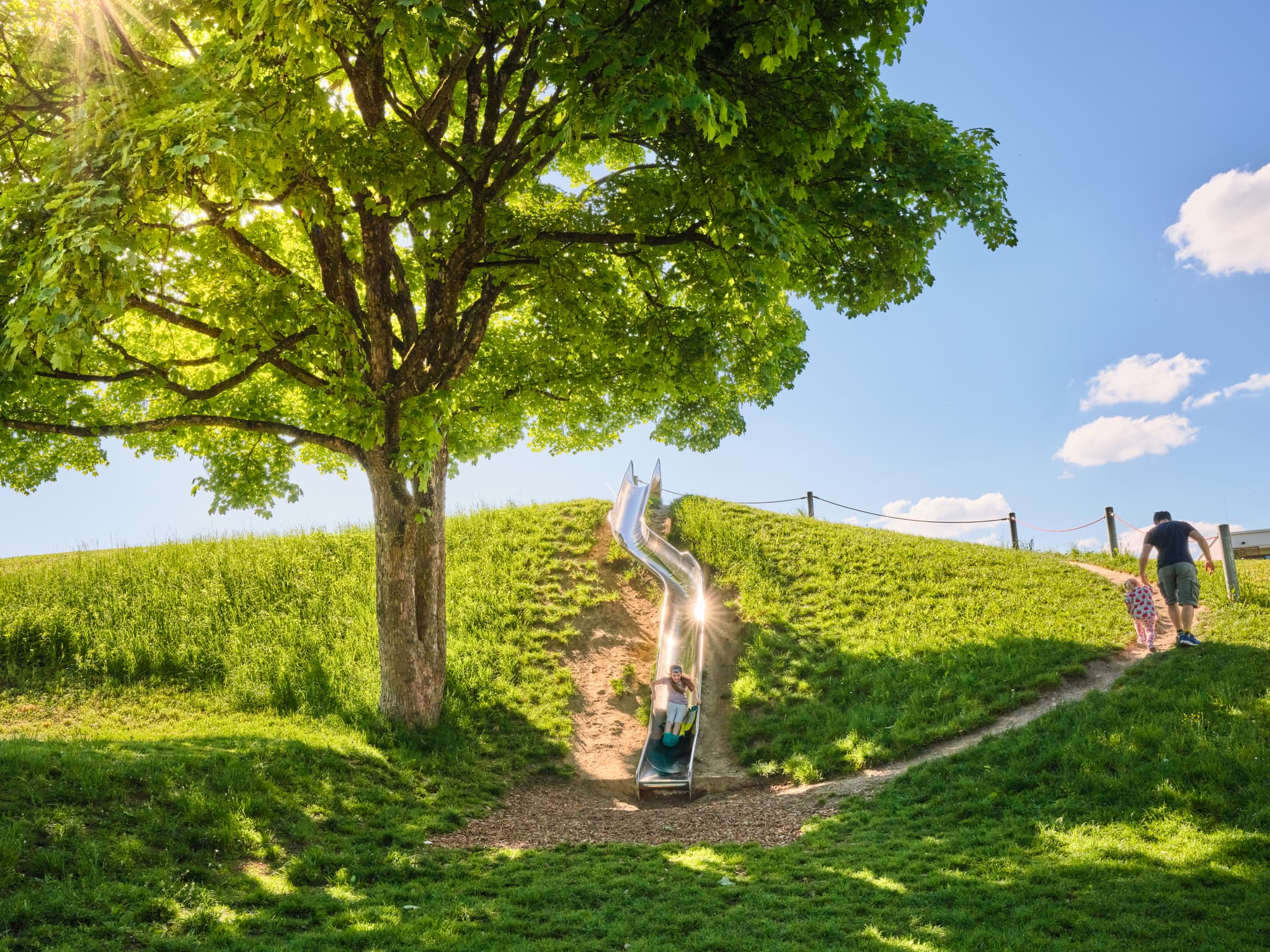 Spielplatz Lindach Motorikpark, Altötting, Oberbayern - Kind auf Rutsche im Lindach Motorikpark, Burghausen, Altötting, Inn-Salzach, Oberbayern. Grüne Hügel mit Baum prägen die Szene in Deutschland.