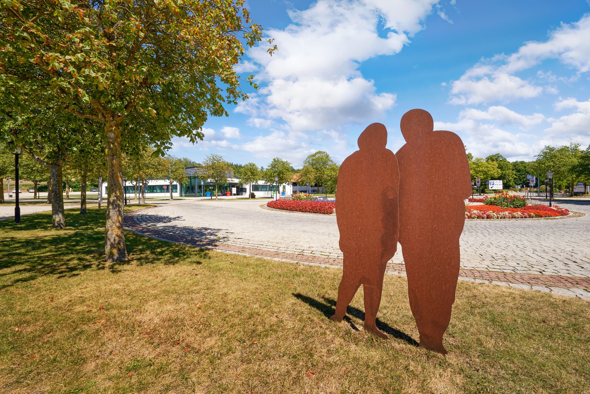 Therme Kreisverkehr, Bad Griesbach, Passau, Niederbayern - Rostige Skulptur am Therme Kreisverkehr in Bad Griesbach, Landkreis Passau. Darstellung eines Paares vor Gebäuden und Grünflächen in Niederbayern, Deutschland.