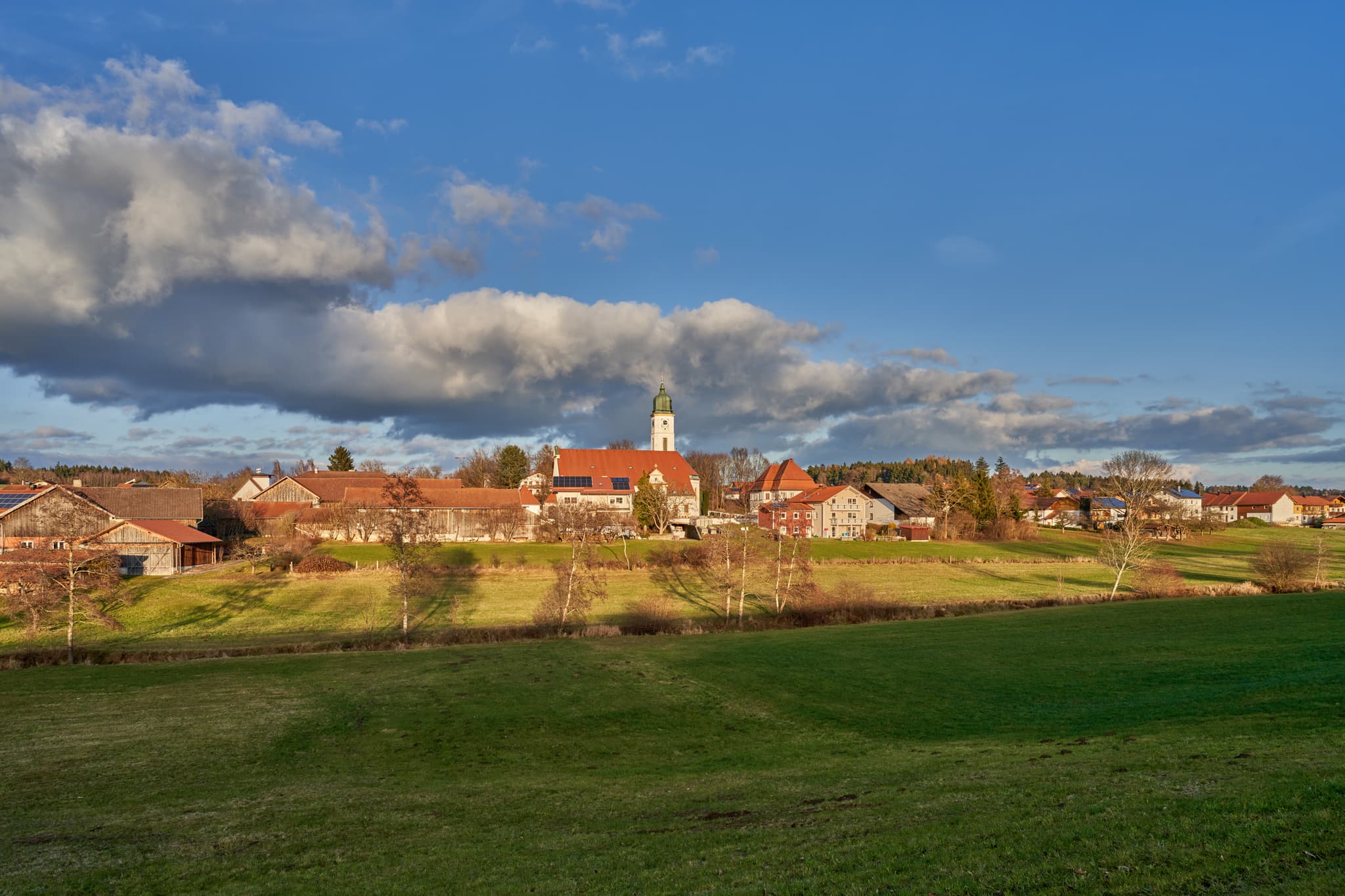 Ulbering, Wittibreut, Rottal-Inn, Niederbayern, Bäderdreieck - Ulbering, Wittibreut, Landkreis Rottal-Inn, Niederbayern. Ländliche Ansicht mit Kirche, Häusern, grünen Wiesen und Bäumen unter blauem Himmel.