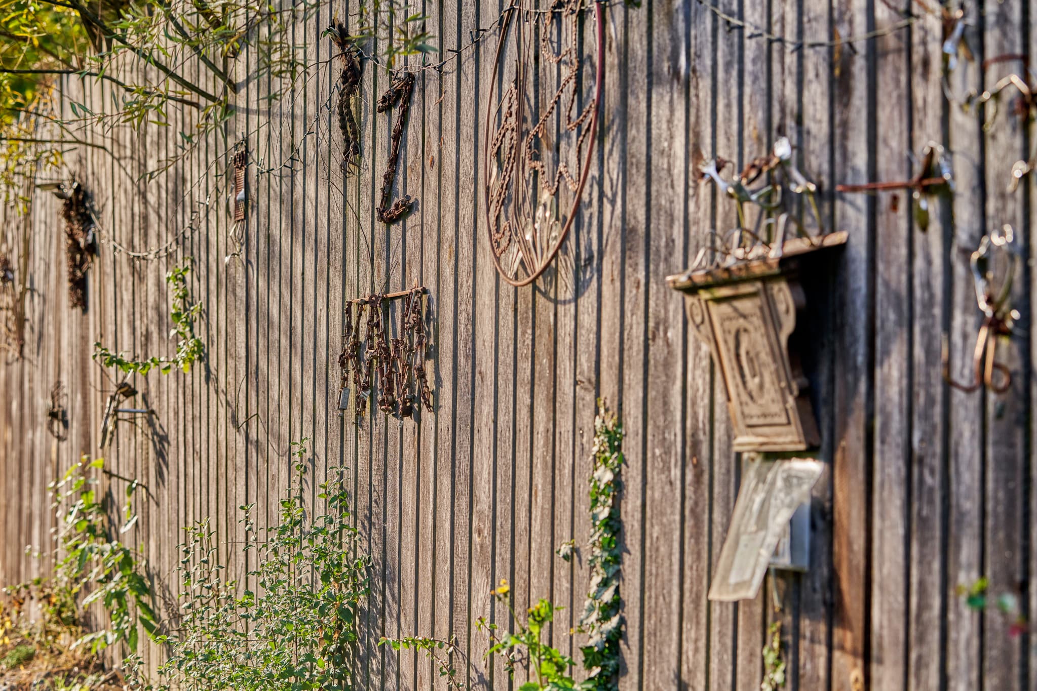 Zaun Hörniweg in Schönau, Rottal-Inn, Niederbayern - Holzzaun am Hörniweg in Schönau, Landkreis Rottal-Inn, Niederbayern. Zeigt  Metallverzierungen und Pflanzen. Hörni-Rätselweg im Bäderdreieck, Deutschland.