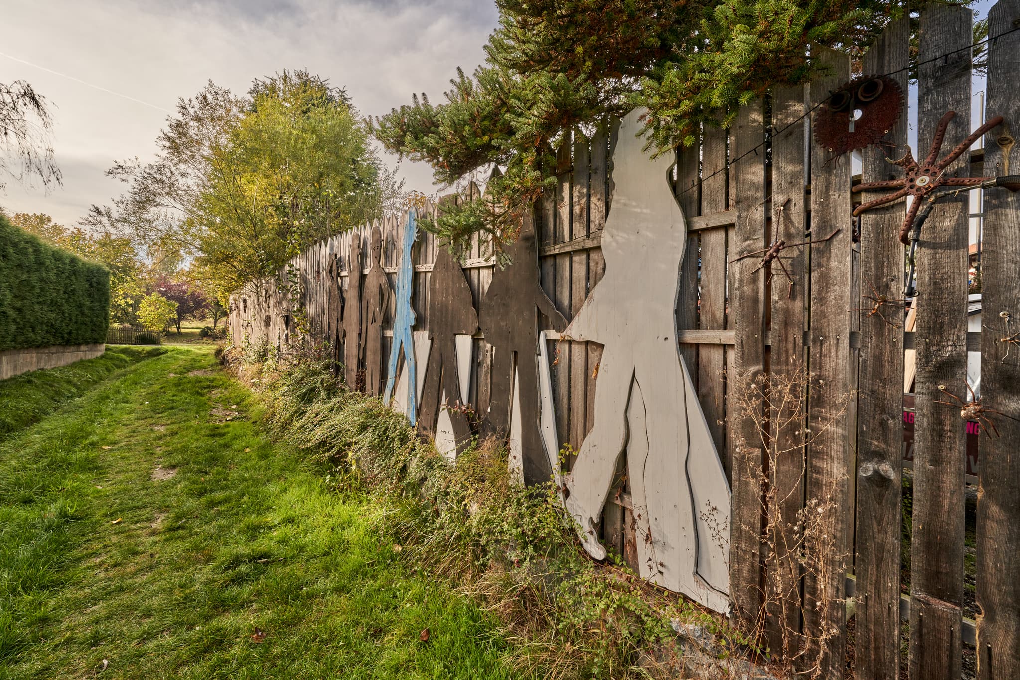 Zaun Hörniweg, Schönau, Rottal-Inn, Niederbayern - Rustikaler Zaun mit Figuren und Spinnen-Objekt am Feldweg in Schönau, Rottal-Inn, Niederbayern. Ländliche Umgebung im Holzland, Deutschland.